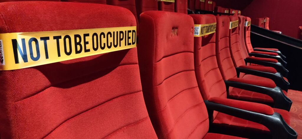 Red theater seats marked for social distancing with 'Not To Be Occupied' tape.