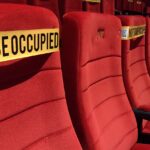 Red theater seats marked for social distancing with 'Not To Be Occupied' tape.