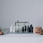 Two players engaged in a focused chess match with chess clock on table.