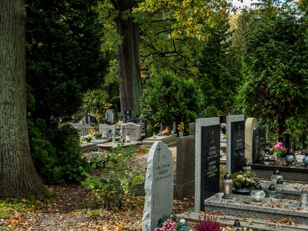 Peaceful cemetery with headstones surrounded by green trees and flowers.