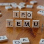 Scrabble tiles spelling IPO and Temu placed on a wooden table surface.