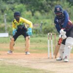Cricket batsman facing bowler with wicketkeeper and fielder outdoors.