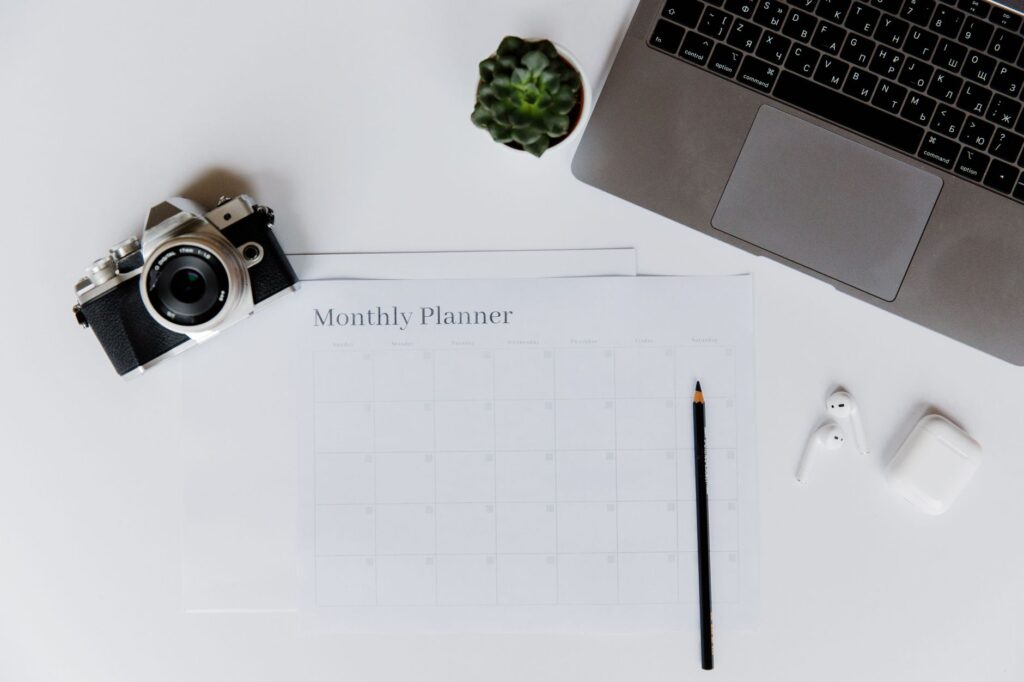 A stylish desk setup featuring a camera, laptop, and monthly planner, perfect for planning and productivity.