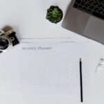A stylish desk setup featuring a camera, laptop, and monthly planner, perfect for planning and productivity.
