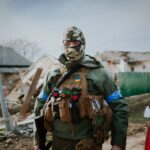Soldier in camouflage gear standing in Kyiv Oblast, Ukraine amidst destruction.