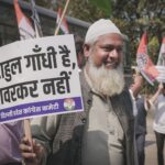 A man participates in a street protest holding a sign with political messaging.