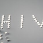 White pills forming the word 'HIV' on a grey background, symbolizing treatment.