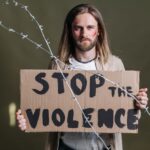 Man holding a 'Stop the Violence' sign with barbed wire emphasizing peace and protest.
