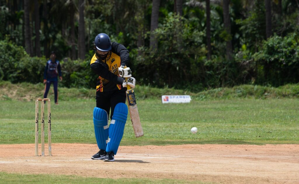 Cricketer making a powerful shot during a day game outdoors.