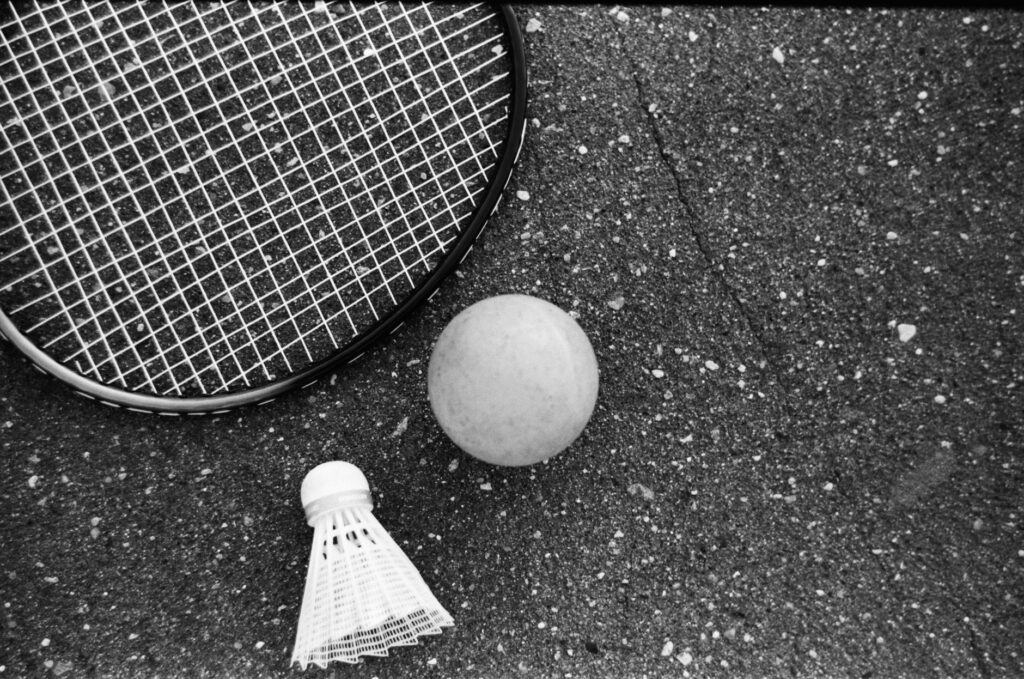 From above of black and white tennis racket with ball and shuttlecock placed on asphalt ground
