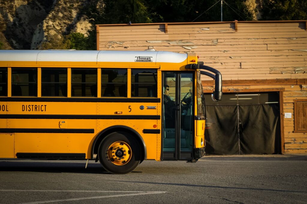 A classic yellow school bus parked on a city street with a rustic wooden building behind it.