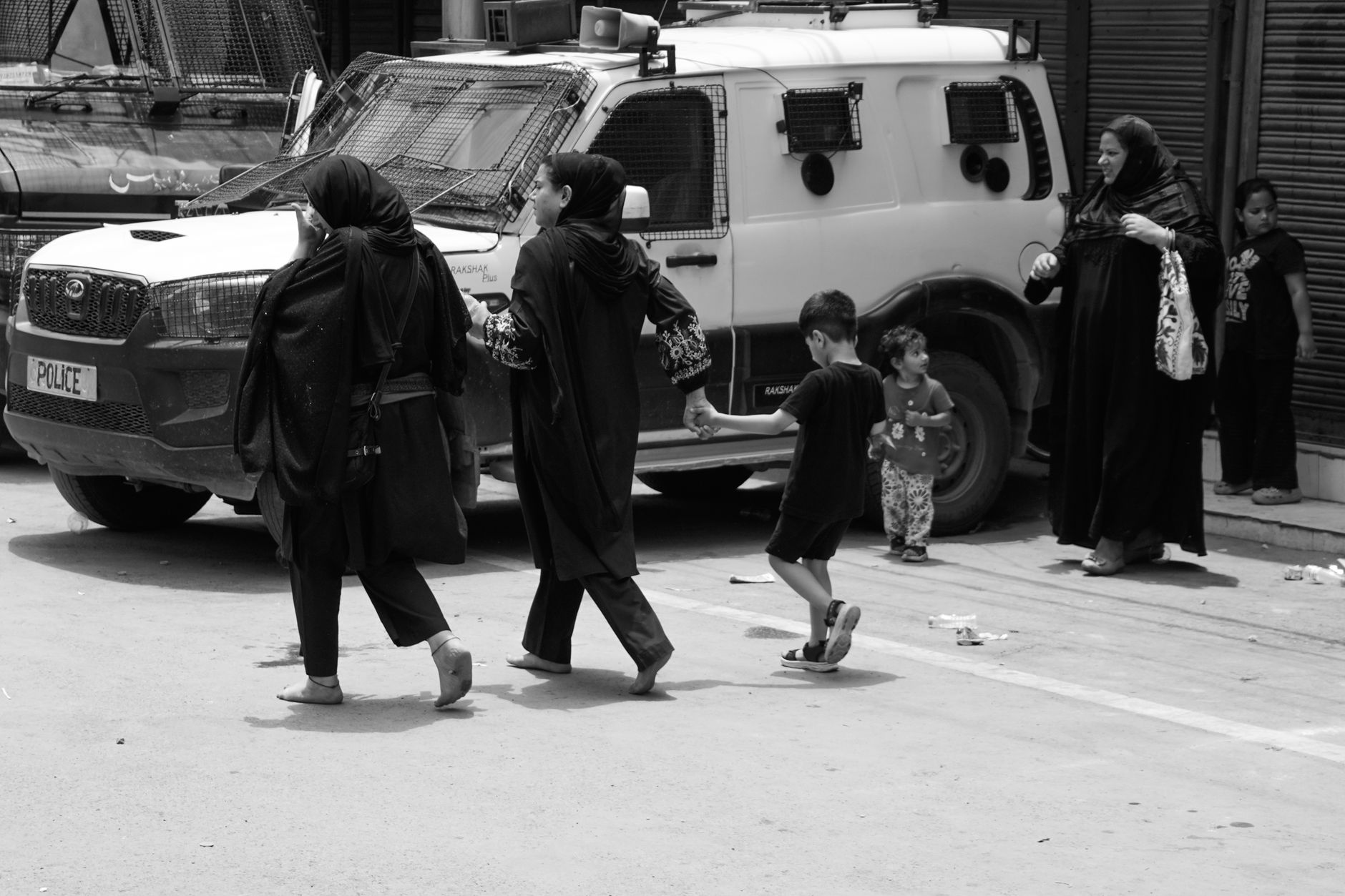 Black and white image capturing people walking past a police vehicle in an urban setting.