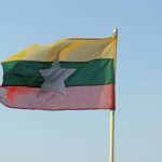 The national flag of Myanmar waving in a clear blue sky, symbolizing freedom and patriotism.
