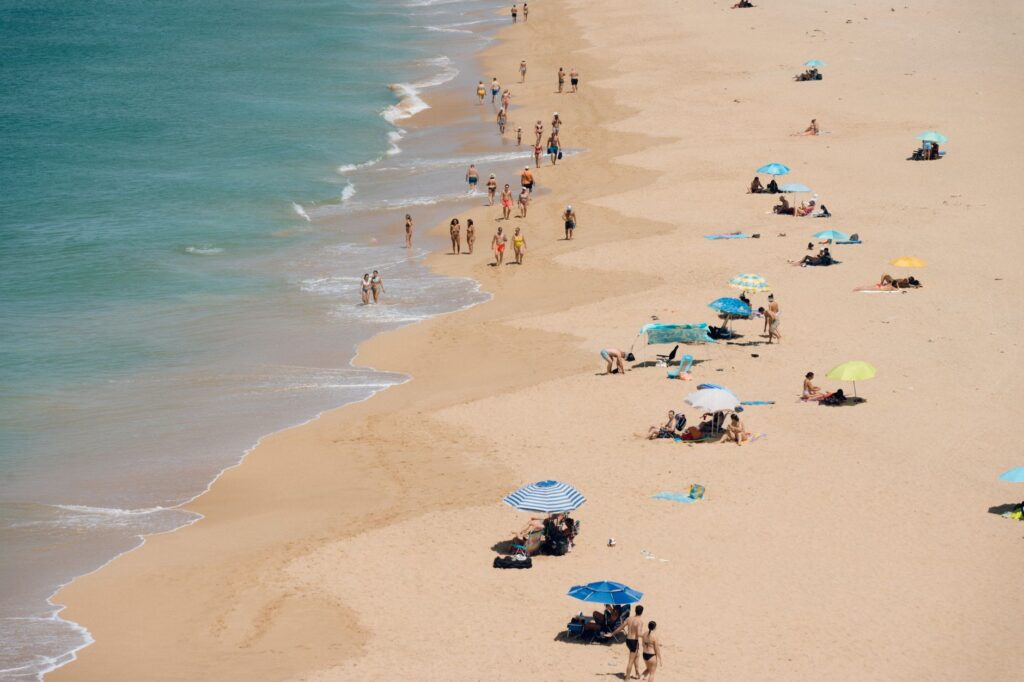 Aerial view of a crowded sandy beach with sunbathers and colorful umbrellas on a sunny day.