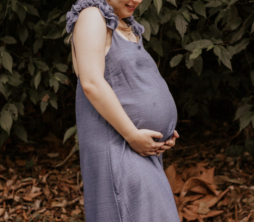 A woman in a blue dress enjoying nature during pregnancy, standing outdoors.