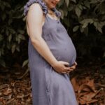 A woman in a blue dress enjoying nature during pregnancy, standing outdoors.