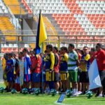 Colorful gathering of diverse soccer teams at a sunlit stadium.