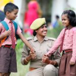 A policewoman smiling and interacting with schoolchildren in uniforms. Outdoors, warm and cheerful scene.