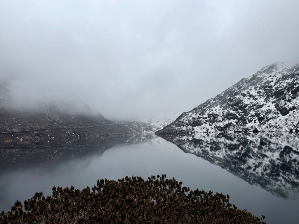 A tranquil winter scene at Tsomgo Lake in Sikkim, with snow-capped mountains mirrored in the water.