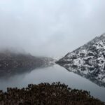 A tranquil winter scene at Tsomgo Lake in Sikkim, with snow-capped mountains mirrored in the water.