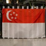The Singapore flag displayed outdoors on a metal fence during the night.