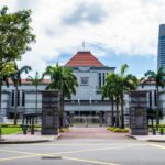 Exterior view of Singapore Parliament House with lush greenery and skyscrapers in the background.