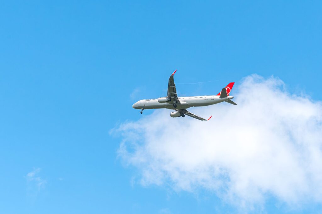 Commercial airplane flying high in the sky with a clear, bright blue backdrop and white clouds.
