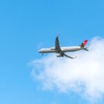 Commercial airplane flying high in the sky with a clear, bright blue backdrop and white clouds.