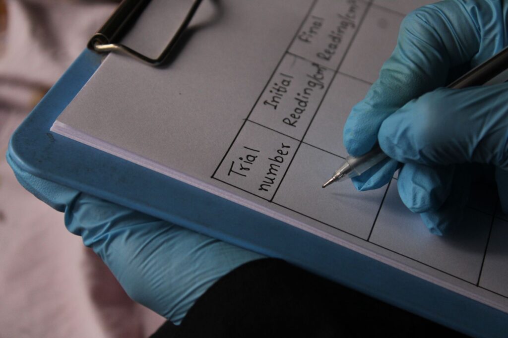 Person wearing gloves writing on clipboard with trial data sheet.