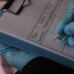 Person wearing gloves writing on clipboard with trial data sheet.