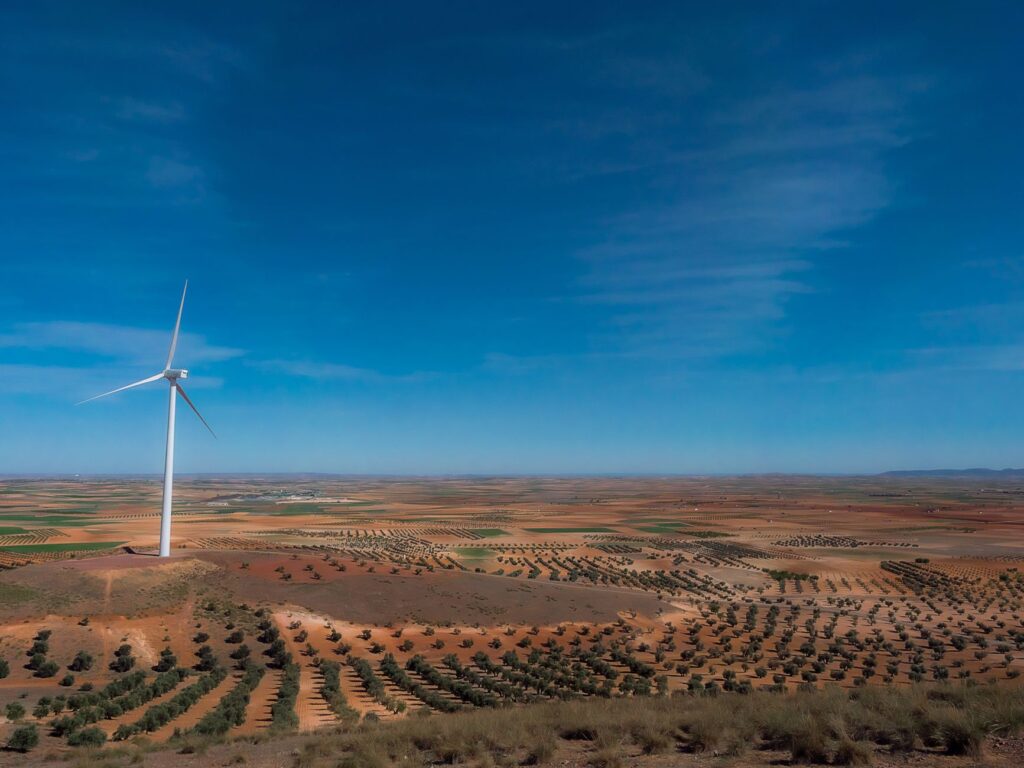 Panoramic view of a wind turbine in a Spanish olive orchard landscape under a clear blue sky.