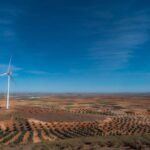 Panoramic view of a wind turbine in a Spanish olive orchard landscape under a clear blue sky.