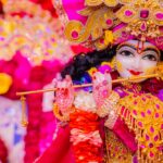 Vibrant Krishna idol adorned with intricate jewelry and flowers holding a flute.