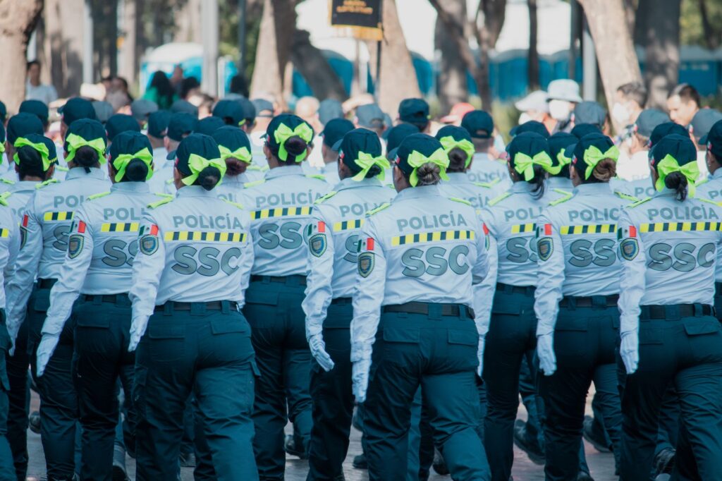 Women police officers in uniform marching in a parade with vibrant green bows in the city.