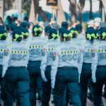 Women police officers in uniform marching in a parade with vibrant green bows in the city.