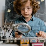 Child using tools like magnifying glass and soldering iron to learn electronics.