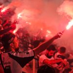 Energetic crowd celebrating with red flares at a sports event, creating a vibrant and passionate atmosphere.