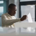 A young man casting his vote at an indoor polling station, focused on the democratic process.