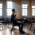 A student raises hand in a university classroom, Buenos Aires, featuring warm light and empty desks.