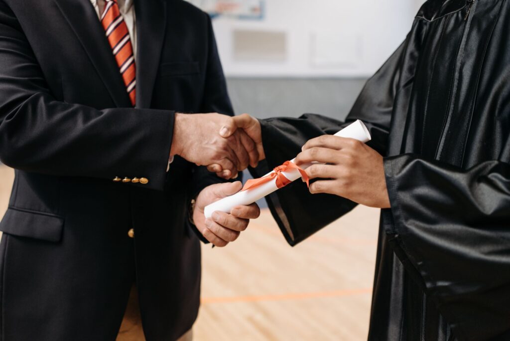 Close-up of a graduate receiving diploma during a graduation ceremony handshake.