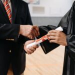 Close-up of a graduate receiving diploma during a graduation ceremony handshake.