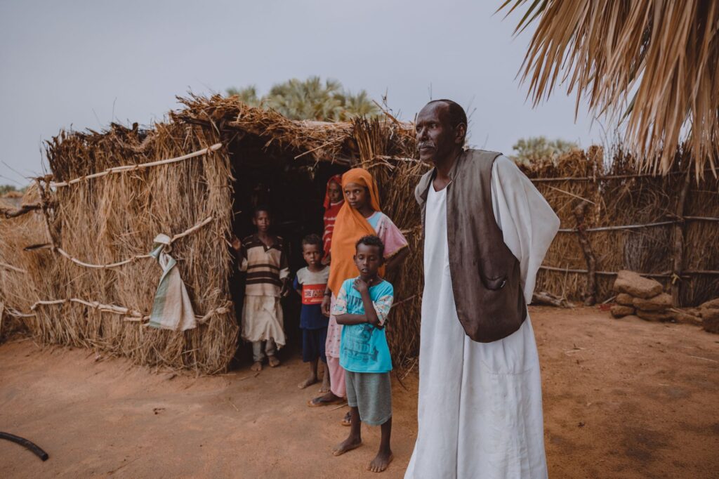 Portrait of family standing outside a traditional straw hut in a rural village.