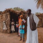 Portrait of family standing outside a traditional straw hut in a rural village.