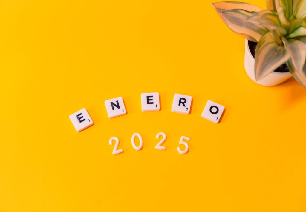Scrabble tiles spelling 'Enero 2025' on a vibrant yellow background with a plant.