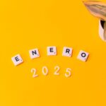 Scrabble tiles spelling 'Enero 2025' on a vibrant yellow background with a plant.