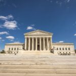 Front view of the United States Supreme Court building on a sunny day with blue sky and clouds.