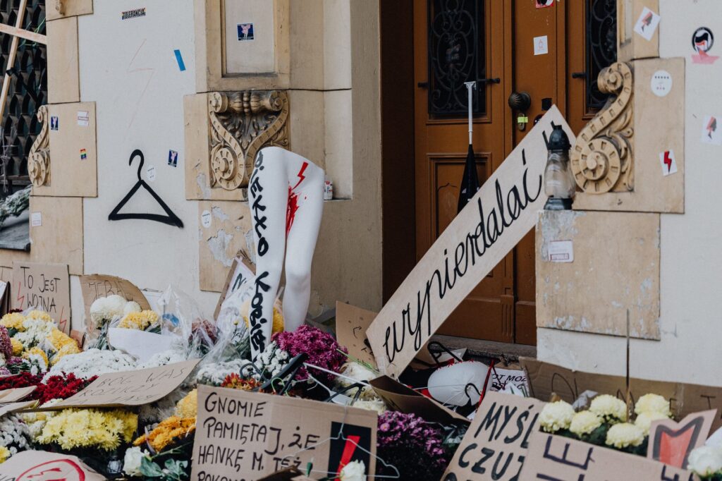 Urban protest scene with flowers and handwritten signs in front of a building, reflecting social activism and public sentiment.