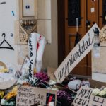 Urban protest scene with flowers and handwritten signs in front of a building, reflecting social activism and public sentiment.