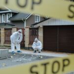 Forensic team examining crime scene with chalk outline and evidence markers outdoors.