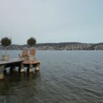 Peaceful pier on Lake Zurich with chairs and potted trees, ideal for relaxation.